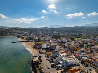 Aerial view of a coastal town where sandy beaches meet the turquoise sea, punctuated by the red-tiled roofs of buildings, Kalyves, Chania, Greece.
