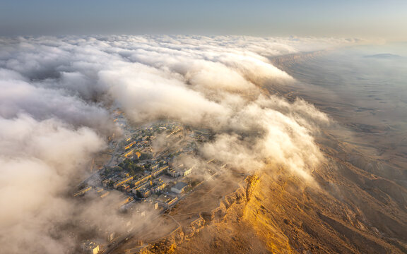 Aerial view of clouds cascading like a waterfall over the desert landscape and the built environment, Mitzpe Ramon, South District, Israel.