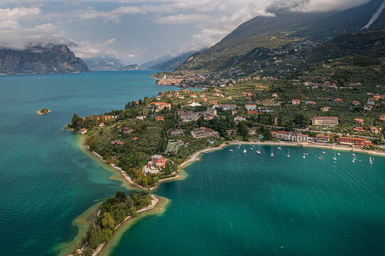 Aerial view of the vibrant turquoise waters embracing the lush green peninsula and the terracotta rooftops of buildings along the shore, Malcesine, Veneto, Italy.