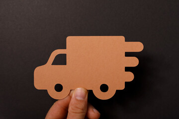 Concept of fast delivery service presented by a truck silhouette on a dark background. Hand holding paper truc