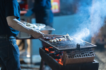 Person grilling street food on outdoor charcoal barbecue