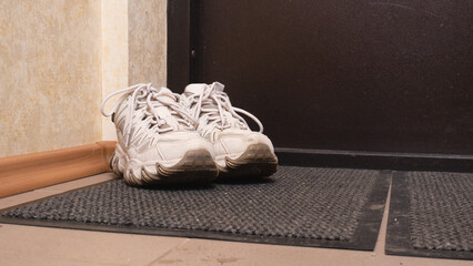 Pair of used sneakers left on doormat, symbolizing need for washing, deodorizing, and household maintenance or cleaning product advertising scenes