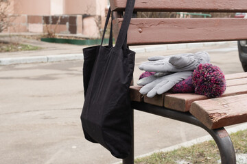 Cloth tote bag hanging from park bench beside warm gloves and knitted hat, illustrating casual winter break outdoors, slow lifestyle, and everyday city living scenes