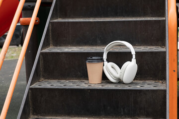 Wireless headphones and takeaway coffee cup resting on metal playground steps, symbolizing short break with music, podcast listening, and modern everyday lifestyle scenes