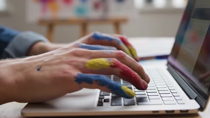 Hands covered in colorful paint typing on laptop keyboard. This engaging scene illustrates creativity and artistic expression, perfect for discussions on art, design, or digital creativity.