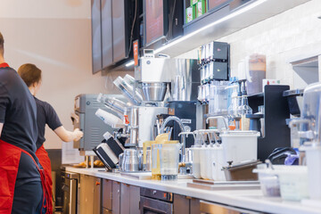 Horizontal wide angle eye level shot of a clean and organized coffee shop prep area with baristas working, featuring various kitchen machines