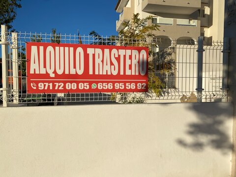 Santa Ponsa, Spain - November 04, 2025: Large red sign displaying "Alquilo Trastero" for storage rental services, prominently placed on a white fence in a sunny urban environment