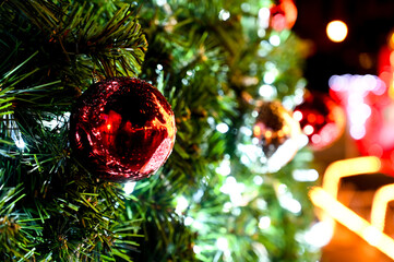 Colorful decorations and string lights on evergreen tree branches. Decorated Christmas tree featuring bright white LED lights and a red bauble ornament 