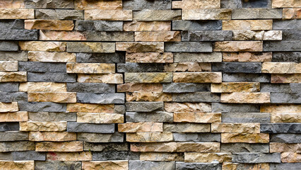 Obraz premium A textured stone wall with a mix of earthy tones and varied stone sizes, viewed from a straight-on perspective.