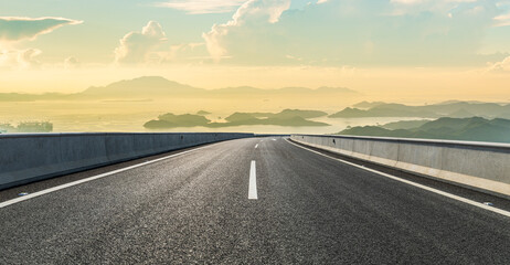 Empty asphalt highway road and beautiful sea with island mountain landscape at sunset