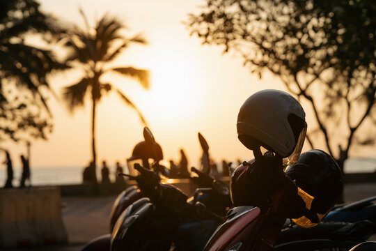 Sea sunset on the coast of Thailand. Motorcycles are parked near the beach as the sun sets in Thailand. Trees line the background with people walking along the shore enjoying the evening. High quality