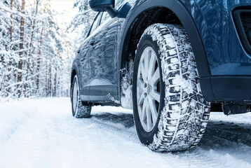 Close-up of a car tire with snow-covered tread on a wintry forest road.