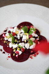 sliced beetroot appetizer on a white plate, goat cheese and fresh herbs, healthy vegetarian food, close-up view, elegant food presentation,
