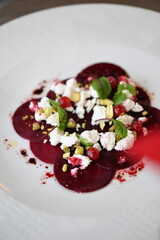 sliced beetroot appetizer on a white plate, goat cheese and fresh herbs, healthy vegetarian food, close-up view, elegant food presentation,