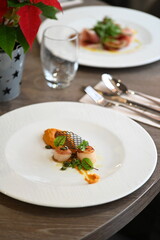 Close-up view of a gourmet appetizer with seared scallops served on a white plate in a fine dining restaurant. Elegant presentation with herbs, sauce, and pur&eacute;e highlights modern European cuisine and 