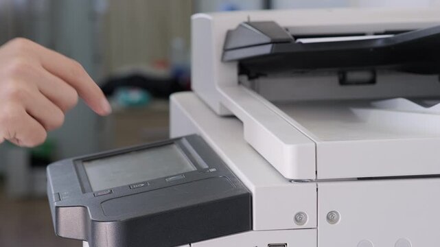 Close-up of person operating modern office copier by pressing touchscreen panel and making photocopies. Office workflow, technology, document management in professional environment