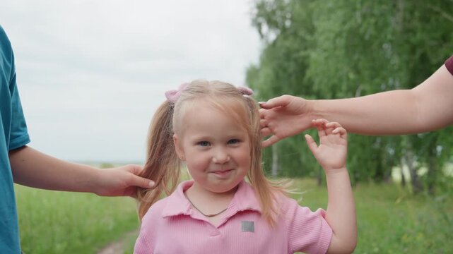 girl giggling in grassy field pink polo ponytail siblings holding hands mother adjusting hair warm family outing candid affectionate moment laughter and playful tug in green meadow
