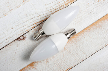 Two LED lamps with E14 sockets lying on a wooden surface.