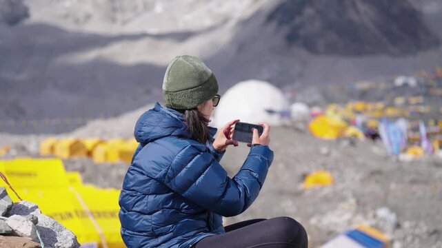 A woman in winter trekking gear sits contemplatively at Everest Base Camp,
