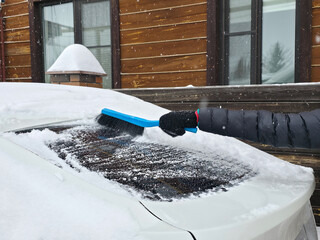 Woman clearing snow from her car windshield during winter. Preparing vehicle for travel in cold weather. Winter season car maintenance.