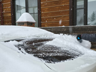 Woman clearing snow from her car windshield during winter. Preparing vehicle for travel in cold weather. Winter season car maintenance.