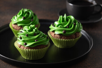 Three chocolate cupcakes with green whipped cream and chocolate sprinkles on dark brown background. St. Patrick's Day. Close up.