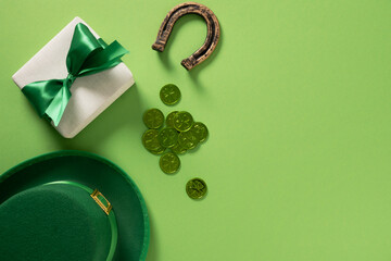 St Patrick's Day frame with gift, Leprechaun hat, horseshoe, shamrock, clover leaves and green coins on light green background. View from above. Copy space.