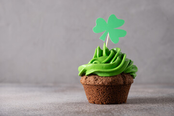 St. Patrick's Day cupcake with green whipped cream decorated clover on gray background. Copy space. Close up. Festive food.