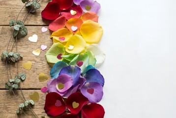 Colorful rose petals and heart confetti arranged on wooden table  