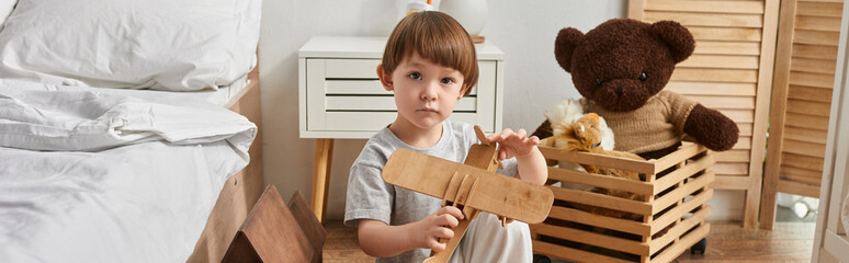 Joyful moments of childhood in a cozy home with a wooden toy airplane, cute little boy