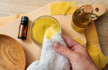 Woman hands apply homemade beeswax wood treatment polish to restore natural wood cutting board. Beeswax, olive oil and essential oil, soft cloth and mixture in glass jar. 