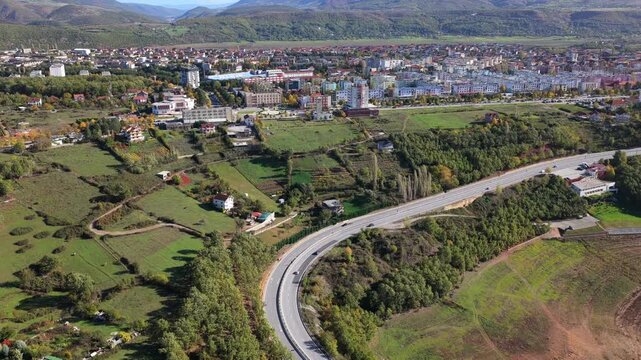 Aerial video of Kuk&euml;s city with residential blocks, surrounding fields, and the A1 Motorway curving through northern Albania landscape. 