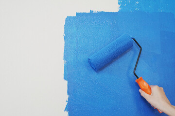 Obraz premium Roller Brush Painting, Worker painting on surface wall Painting apartment, renovating with blue color paint. Leave empty copy space white to write descriptive text beside. 