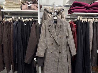 A classic plaid coat is displayed among neatly organized neutral toned garments in a fashion retail store