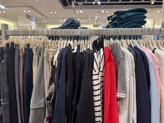 A full rack of mixed casual clothing in neutral and accent colors is displayed in a bright modern fashion store