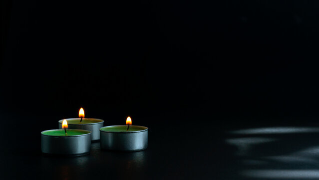 Multiple burning tealight candles arranged in a row against a dark background, symbolizing remembrance, peace, spirituality, unity, and calm atmosphere with copy space. - Powered by Adobe