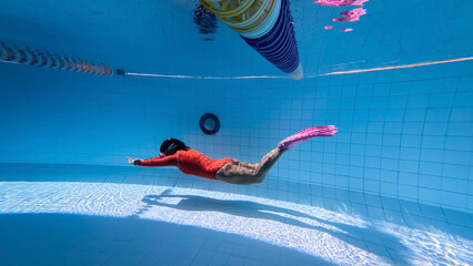 Young woman with mermaid tail swims and dives under sunlit deep water