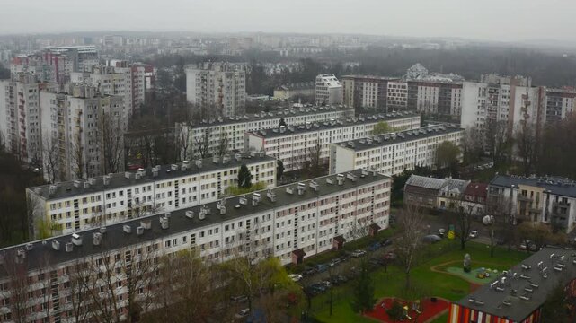 Aerial shot of eastern european residential apartment blocks in Krakow, dense urban housing, rooftops and parks under overcast skies and light fog - slow pan left.