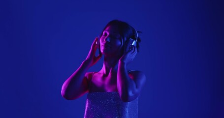 A woman wearing headphones, immersed in music, is illuminated by vibrant purple and blue neon lights. Slow motion.
