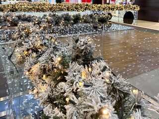 Snow covered Christmas garland with warm lights along glass railing in modern shopping mall interior. Seasonal decoration, festive atmosphere, winter celebration, public space design and holiday