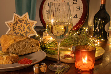 Obraz premium a festive New Year's Eve table setting featuring a wine glass refracting a clock face, accompanied by rustic bread with red caviar, a lit candle, and sparkling fairy lights.