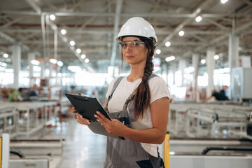 Female engineer is with notepad. Woman is in the window making factory