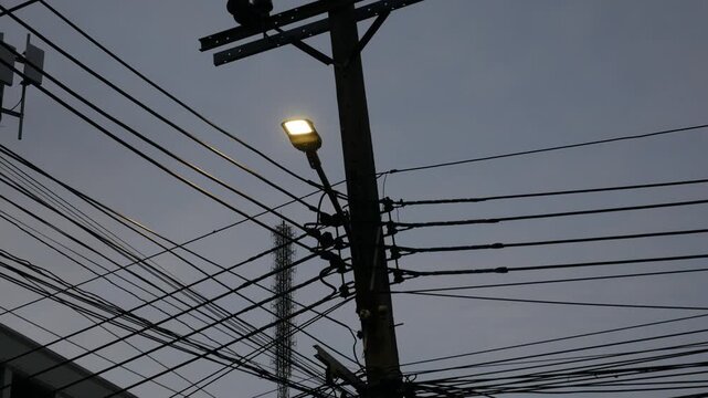 Dense tangle of utility wires and cables forming a busy silhouette around a wooden pole against a deep blue evening sky, urban electric infrastructure complexity.