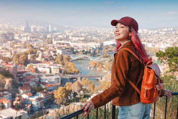 Woman with backpack admiring the panoramic cityscape of Tbilisi, Georgia, from a high viewpoint, experiencing travel and tourism © EdNurg