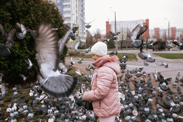 Senior woman feeding pigeons in city. Gentle human-animal connection and quiet city life. Everyday urban moment.