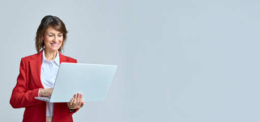 Middle-aged professional latin hispanic business lady in red suit working on laptop pc isolated. 40s mature office worker woman using computer technology for analysing work. Web banner, copy space