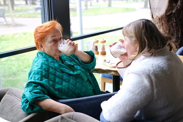 Two Diverse Young Women Enjoying a Meal and Drinks Together at a Cozy Cafe by the Window on a Bright Afternoon. High quality photo