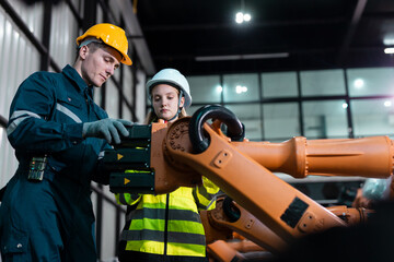 Engineers wearing safety helmets inspecting robotic arms in smart factory, using digital tablet to review automation processes, symbolizing industrial innovation and teamwork.
