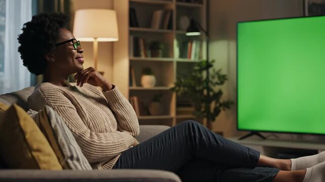 woman watching a green screen TV on the couch, Cozy living room setup with a minimalist wooden TV stand and shelf