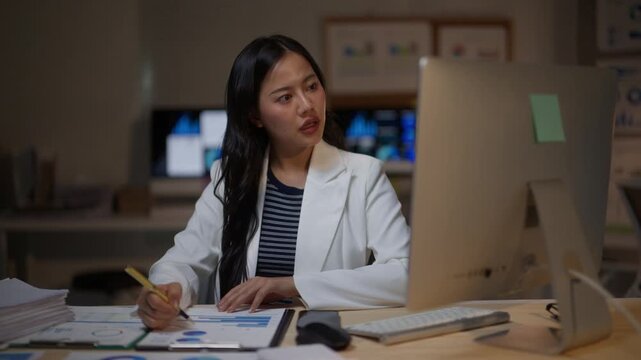Young asian businesswoman feeling stressed and tired while working overtime in the office at night. She is analyzing financial data